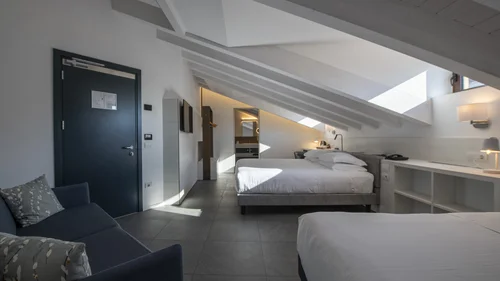Boutique Hotel a Verona · Touring 3★ · A 2 min da Piazza Erbe Camera d'hotel mansardata con due letti, divano e luce naturale dalle finestre sul tetto