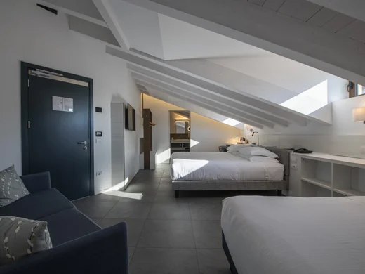 Boutique Hotel a Verona · Touring 3★ · A 2 min da Piazza Erbe Camera d'hotel mansardata con due letti, divano e luce naturale dalle finestre sul tetto